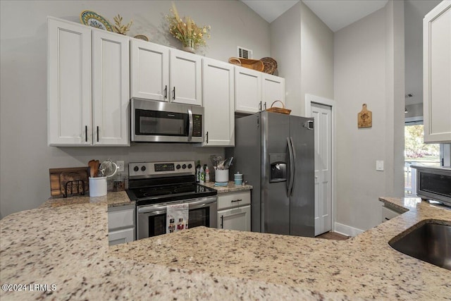 kitchen with lofted ceiling, sink, light stone counters, appliances with stainless steel finishes, and white cabinets