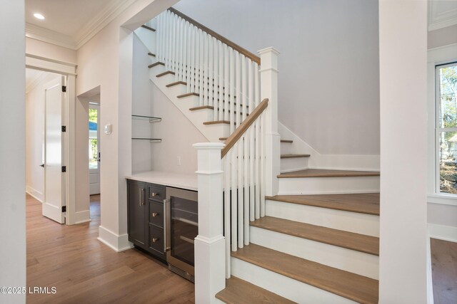 stairway with plenty of natural light, ornamental molding, beverage cooler, and wood-type flooring