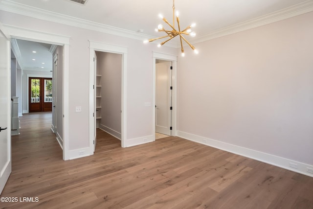 unfurnished bedroom featuring hardwood / wood-style floors, a chandelier, a walk in closet, crown molding, and a closet