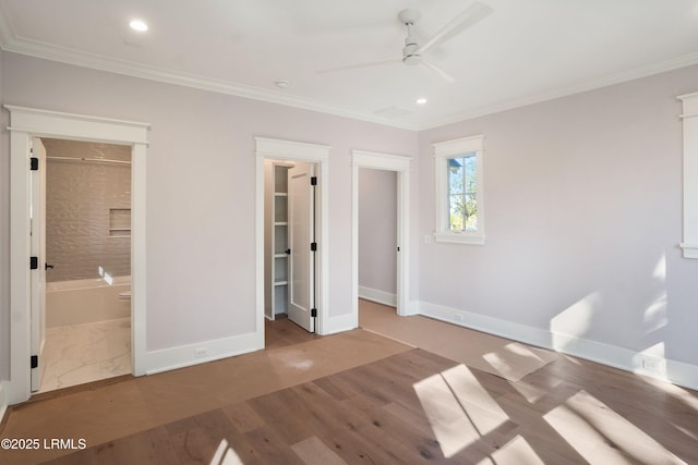 unfurnished bedroom with ensuite bathroom, hardwood / wood-style flooring, ornamental molding, a walk in closet, and ceiling fan