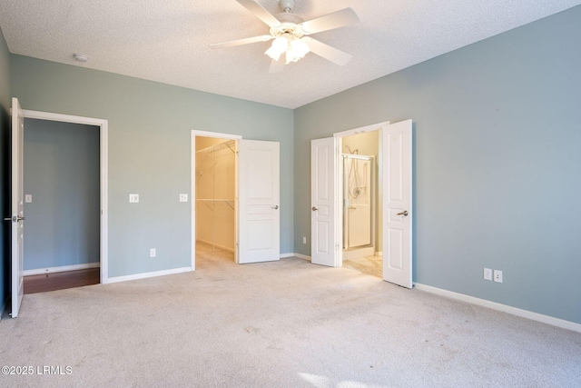 unfurnished bedroom with ceiling fan, a textured ceiling, a spacious closet, light colored carpet, and a closet