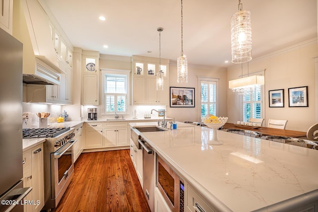 kitchen featuring light stone counters, decorative light fixtures, stainless steel appliances, and a center island with sink