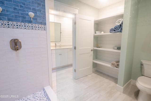 bathroom featuring a tile shower, vanity, and toilet