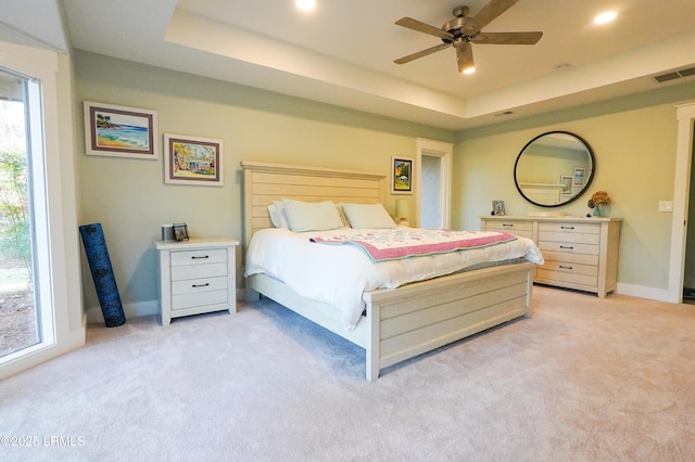 bedroom featuring a tray ceiling, light colored carpet, and visible vents