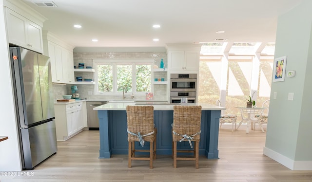 kitchen with a kitchen island, white cabinetry, light countertops, appliances with stainless steel finishes, and open shelves