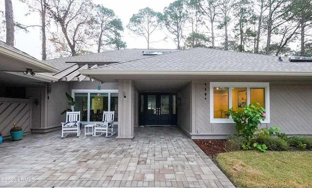 rear view of property with french doors, a shingled roof, and a patio