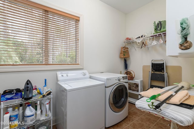 clothes washing area featuring dark tile patterned flooring, washer and clothes dryer, and a healthy amount of sunlight