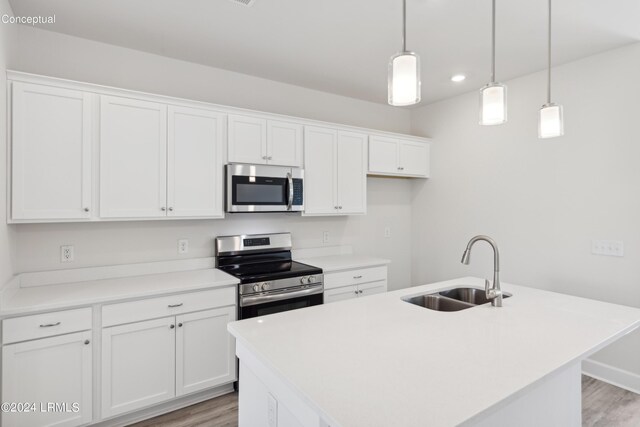 kitchen with light wood finished floors, white cabinets, appliances with stainless steel finishes, hanging light fixtures, and a sink