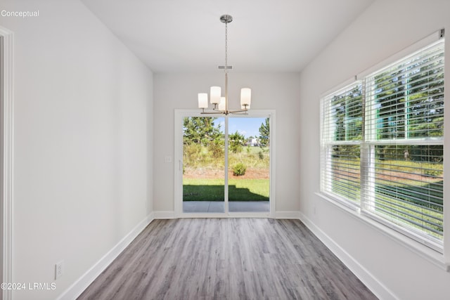 unfurnished dining area featuring baseboards, a chandelier, and wood finished floors