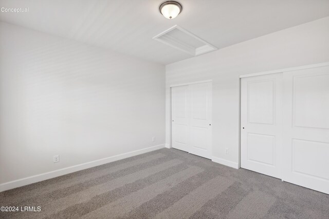 unfurnished bedroom with attic access, carpet floors, baseboards, and multiple closets