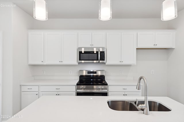 kitchen featuring decorative light fixtures, stainless steel appliances, light countertops, white cabinets, and a sink