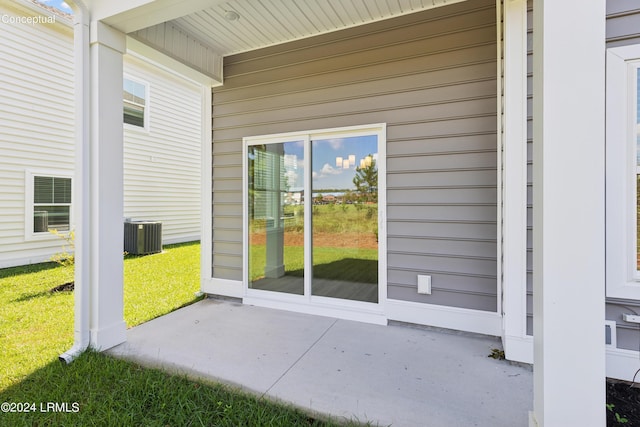 property entrance featuring central air condition unit, a patio area, and a lawn