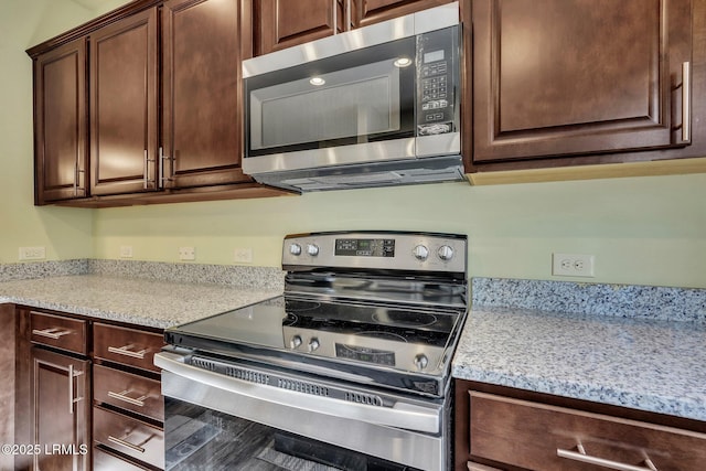 kitchen featuring stainless steel appliances, dark brown cabinetry, and light stone counters