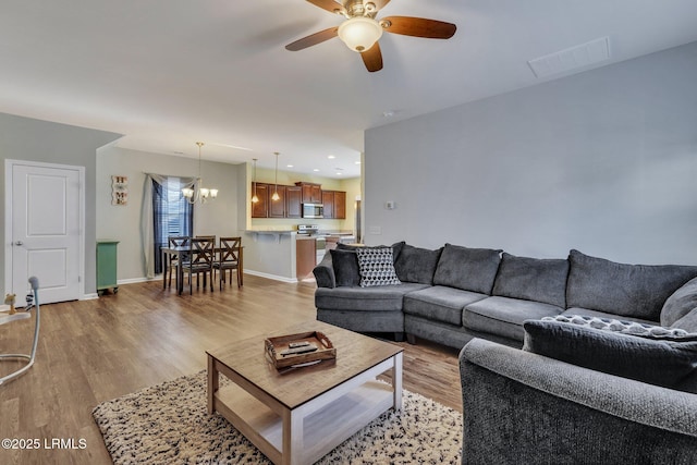 living room featuring ceiling fan with notable chandelier and light hardwood / wood-style floors