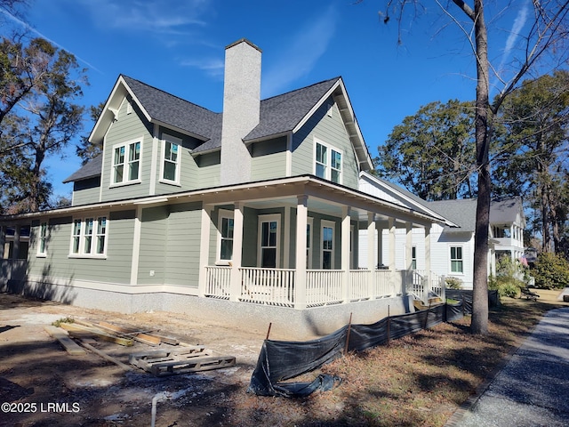 exterior space featuring a shingled roof, a porch, and a chimney