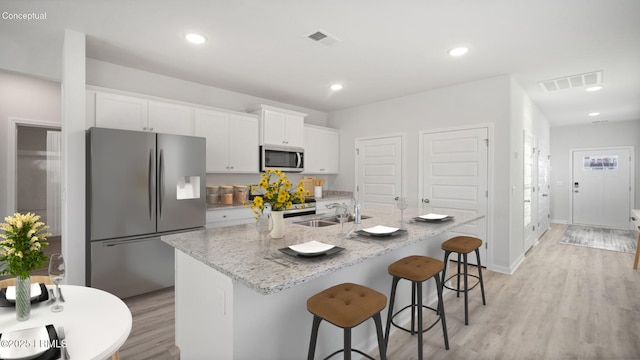 1533 Sanctum St, Ridgeland, SC 29936 - kitchen with stainless steel appliances, light wood finished floors, white cabinetry, a center island with sink, and light stone counters