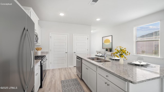 1533 Sanctum St, Ridgeland, SC 29936 - kitchen with appliances with stainless steel finishes, a center island with sink, white cabinets, light wood-style flooring, and light stone counters