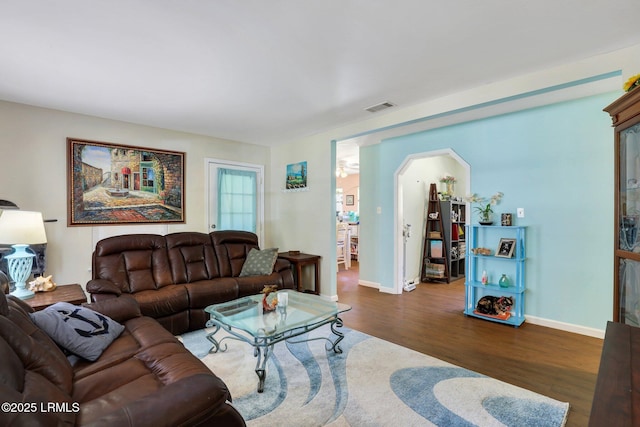 living room featuring arched walkways, wood finished floors, visible vents, and baseboards