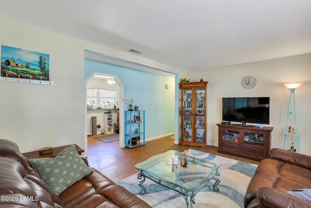 living room featuring visible vents, baseboards, arched walkways, and wood finished floors