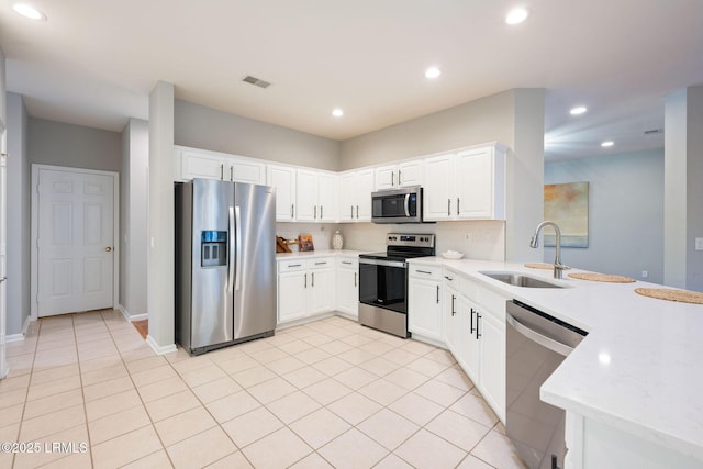 kitchen with appliances with stainless steel finishes, white cabinetry, sink, backsplash, and light tile patterned floors