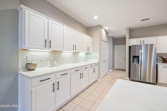 kitchen with white cabinetry, light tile patterned floors, stainless steel fridge, and backsplash