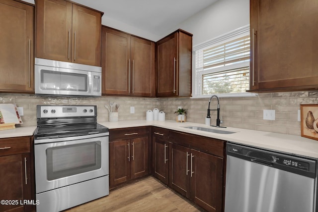 kitchen with tasteful backsplash, appliances with stainless steel finishes, light hardwood / wood-style floors, and sink