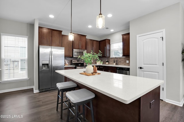 kitchen featuring appliances with stainless steel finishes, a center island, dark brown cabinetry, dark hardwood / wood-style flooring, and decorative light fixtures