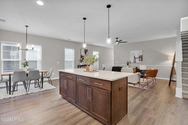 kitchen featuring dark brown cabinetry, wood-type flooring, decorative light fixtures, a center island, and ceiling fan with notable chandelier