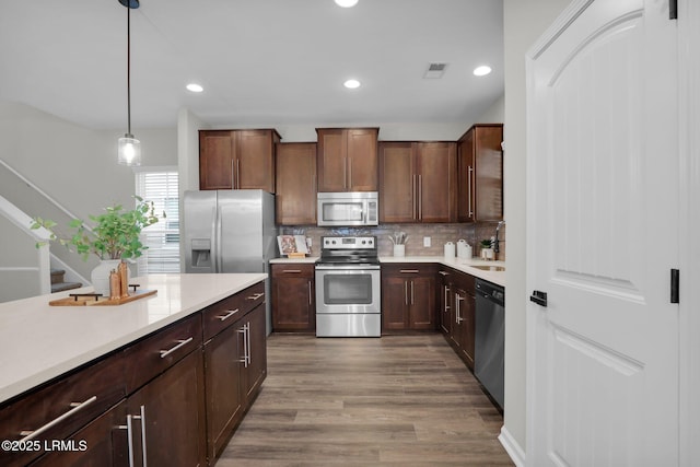 kitchen with sink, hardwood / wood-style flooring, appliances with stainless steel finishes, hanging light fixtures, and decorative backsplash