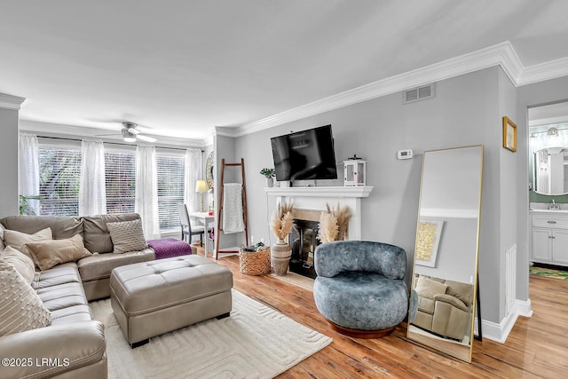 living room with crown molding, visible vents, a glass covered fireplace, light wood-type flooring, and baseboards