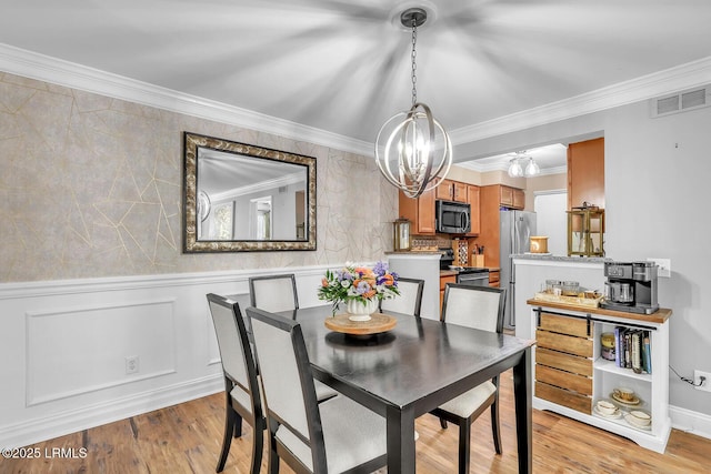 dining area featuring light wood-style flooring, a decorative wall, visible vents, wainscoting, and crown molding