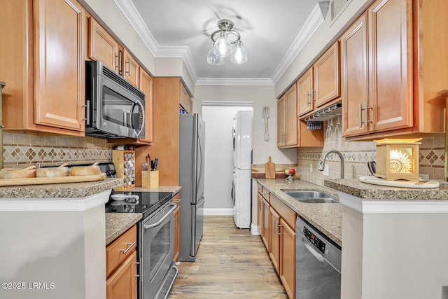 kitchen with appliances with stainless steel finishes, ornamental molding, stacked washer / drying machine, light wood-type flooring, and a sink