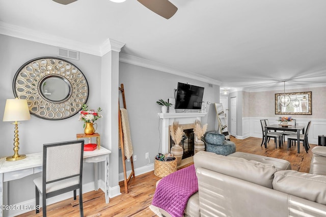 living area featuring visible vents, wainscoting, a premium fireplace, wood finished floors, and crown molding