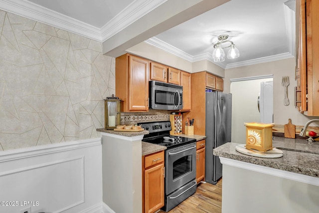 kitchen with appliances with stainless steel finishes, brown cabinetry, a sink, and crown molding