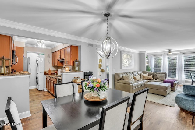 dining area with stacked washer / drying machine, visible vents, ornamental molding, light wood-type flooring, and ceiling fan with notable chandelier