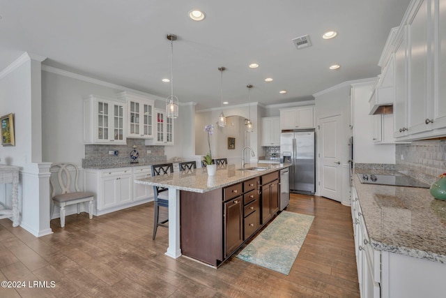 kitchen featuring appliances with stainless steel finishes, decorative light fixtures, white cabinetry, sink, and a center island with sink