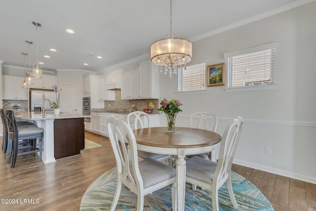 dining space with sink, hardwood / wood-style flooring, ornamental molding, and a chandelier