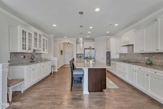 kitchen featuring white cabinetry, hanging light fixtures, a kitchen island with sink, and custom range hood