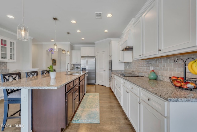 kitchen with stainless steel appliances, white cabinetry, a kitchen island with sink, and a kitchen bar