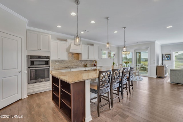 kitchen with a breakfast bar, pendant lighting, white cabinetry, sink, and a spacious island