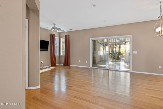 unfurnished living room featuring ceiling fan with notable chandelier, baseboards, and light wood-type flooring