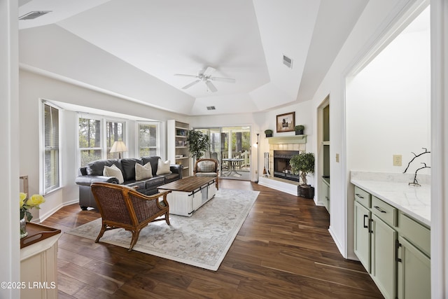 living room with a tile fireplace, dark hardwood / wood-style floors, ceiling fan, and a tray ceiling