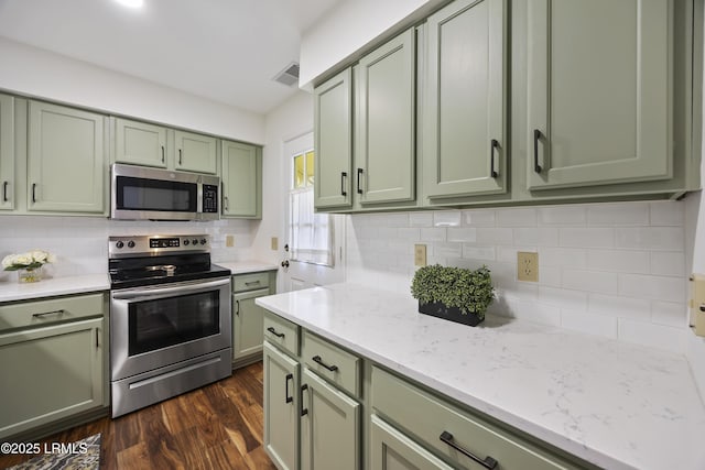 kitchen featuring appliances with stainless steel finishes, tasteful backsplash, green cabinets, light stone countertops, and dark wood-type flooring