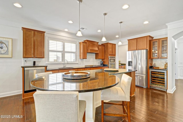 kitchen featuring a kitchen island, appliances with stainless steel finishes, pendant lighting, sink, and beverage cooler