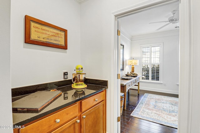 kitchen with crown molding, dark hardwood / wood-style floors, dark stone counters, and ceiling fan