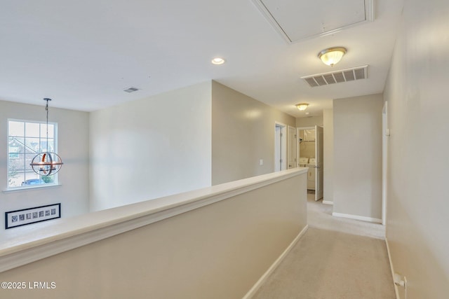 hallway with attic access, visible vents, light carpet, and baseboards