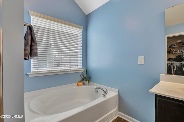 bathroom with lofted ceiling, a garden tub, vanity, and baseboards