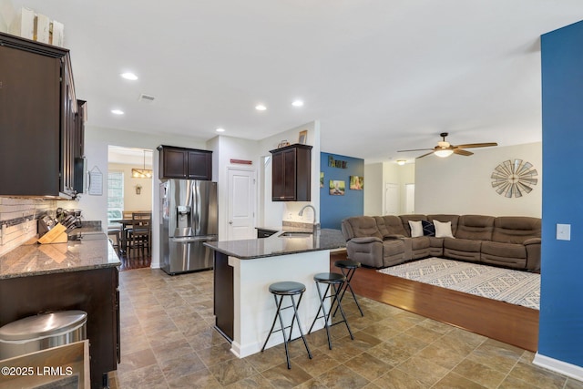 kitchen featuring a peninsula, a sink, open floor plan, stainless steel refrigerator with ice dispenser, and a kitchen bar