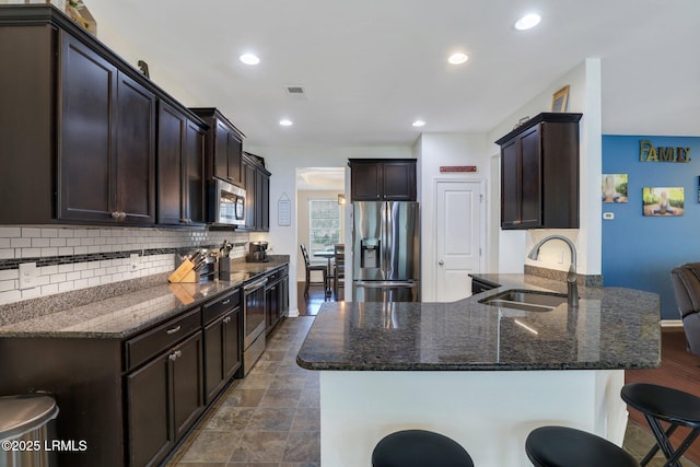 kitchen with stainless steel appliances, a sink, dark brown cabinets, tasteful backsplash, and a kitchen bar