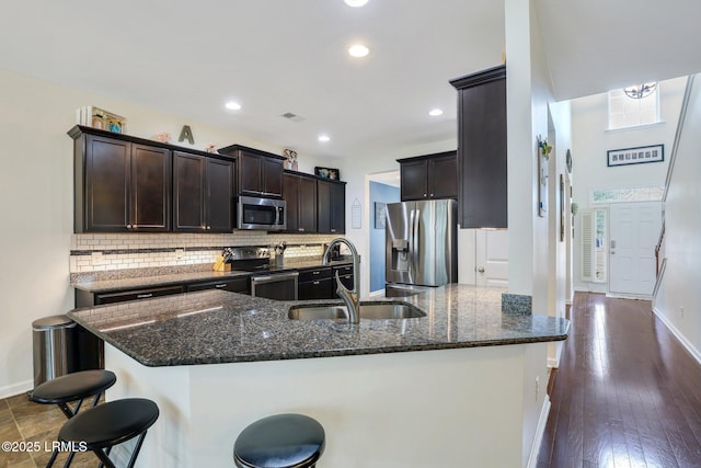 kitchen with a breakfast bar area, stainless steel appliances, a sink, dark stone counters, and tasteful backsplash